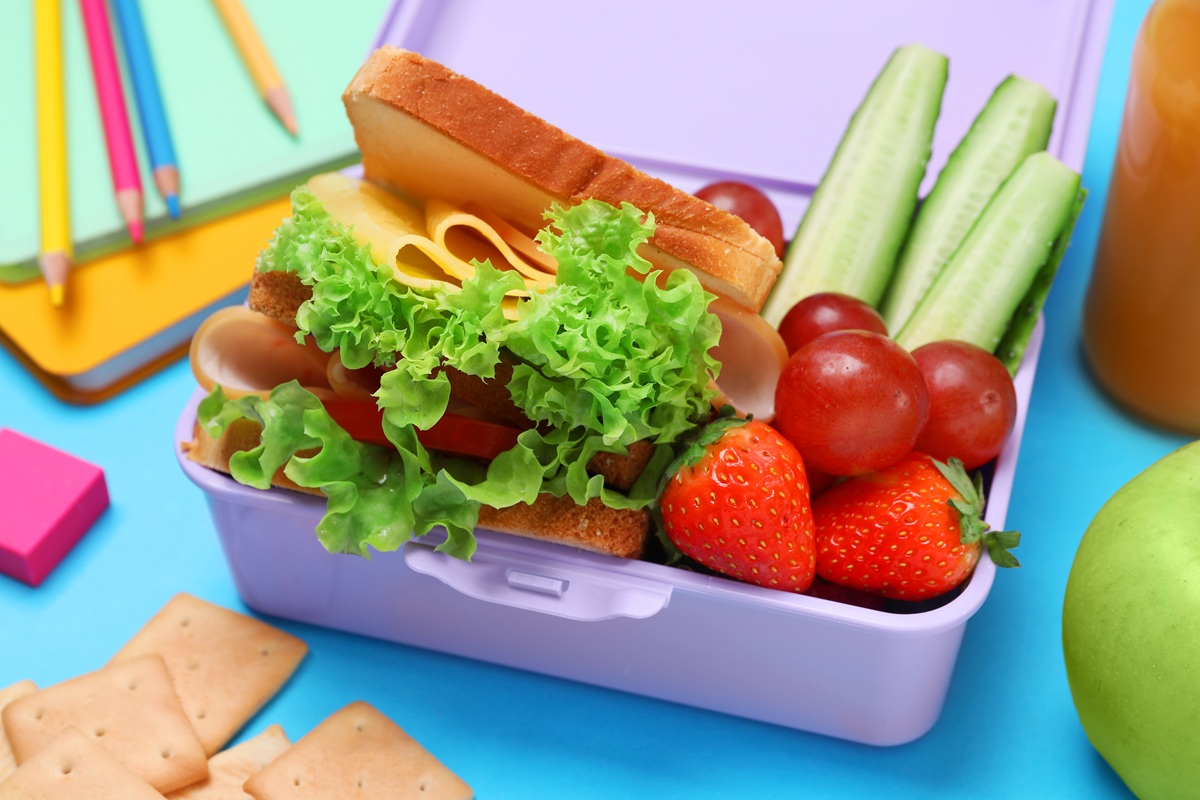 Lunchbox with tasty food and school stationery on light blue background, closeup
